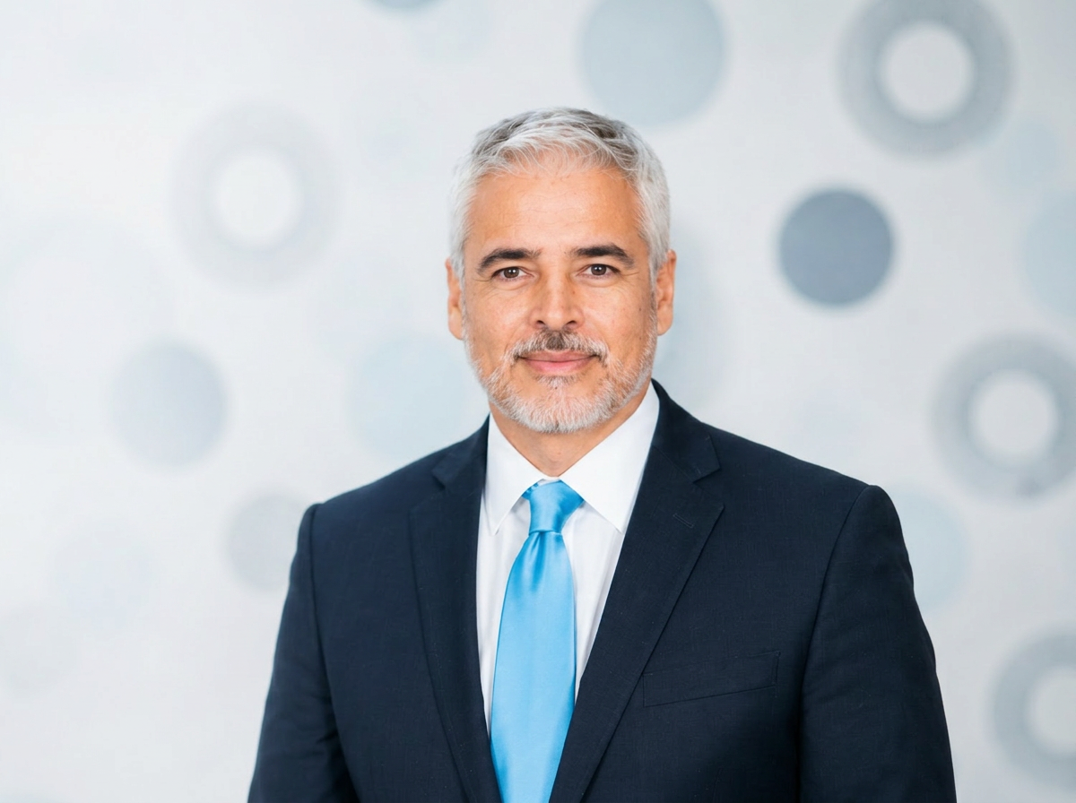 Portrait of Dr. Ariel Ortiz in a navy suit against a soft light background with subtle blue ring motifs.